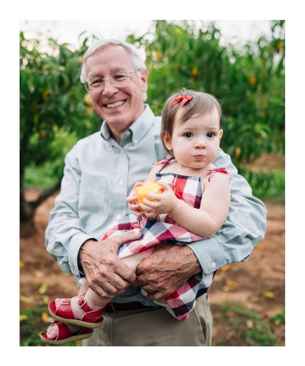 grandfather holding baby in peach orchard